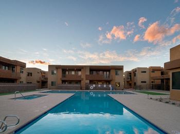 An apartment complex with a swimming pool in the foreground and apartments in the background